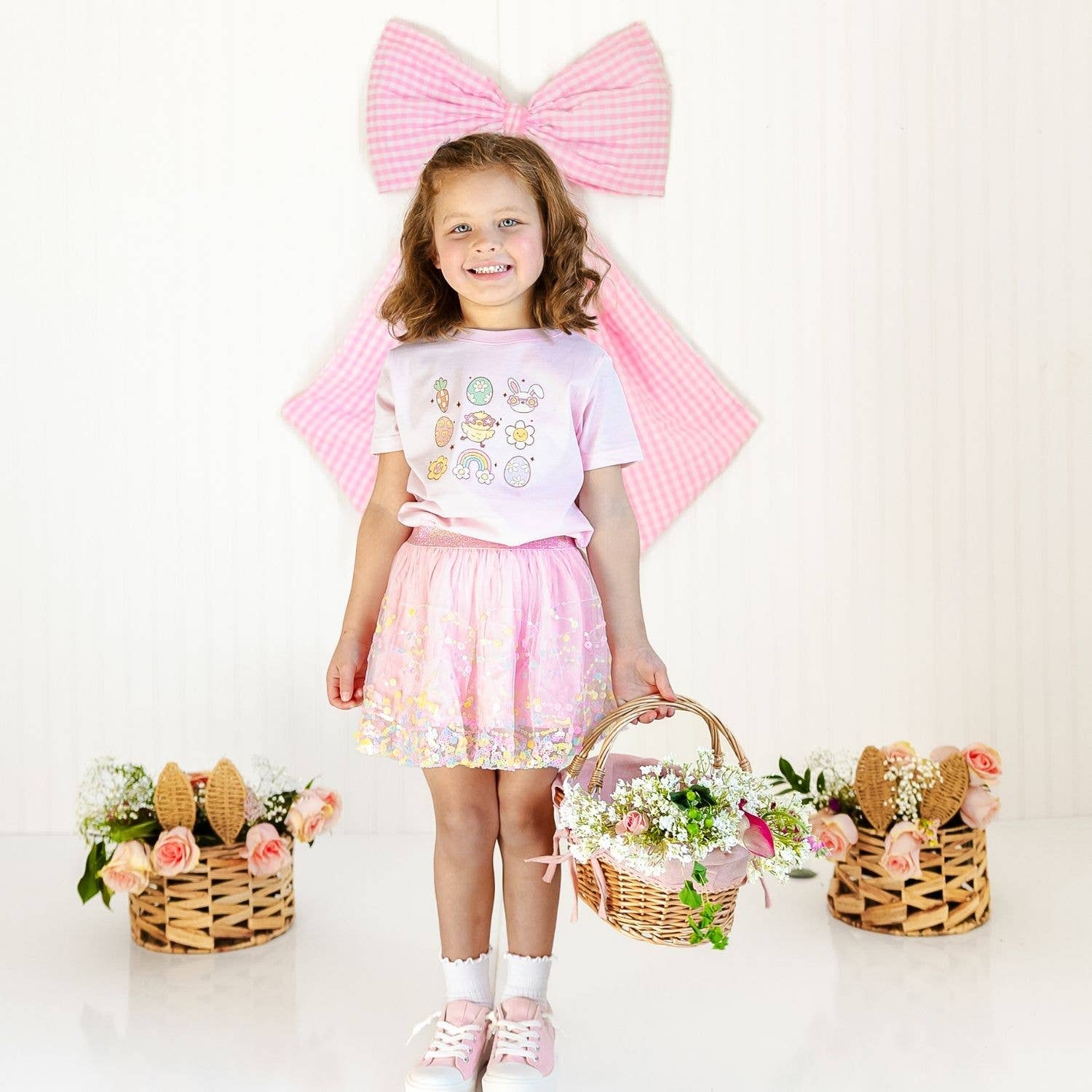 Young girl in a pink outfit with a large bow and Easter baskets on a white background