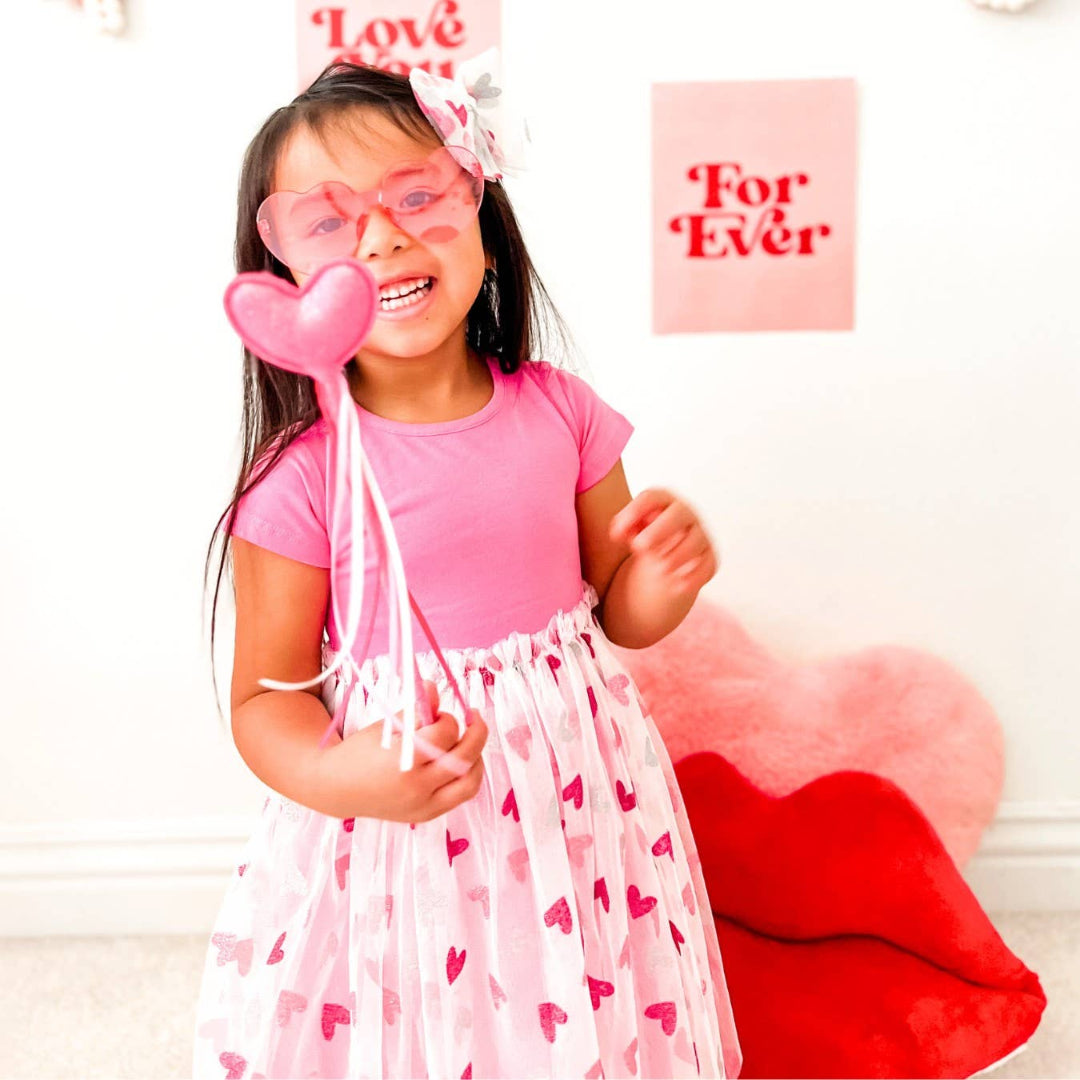 little girl holding a pink glittery wand with a heart on the top and streamers hanging down