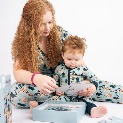 mother and son, who are both decked out in their "pirate's life" pajamas; mom in the women's top and joggers, and the baby in the convertible, play with the "pirate's life" puzzle. 