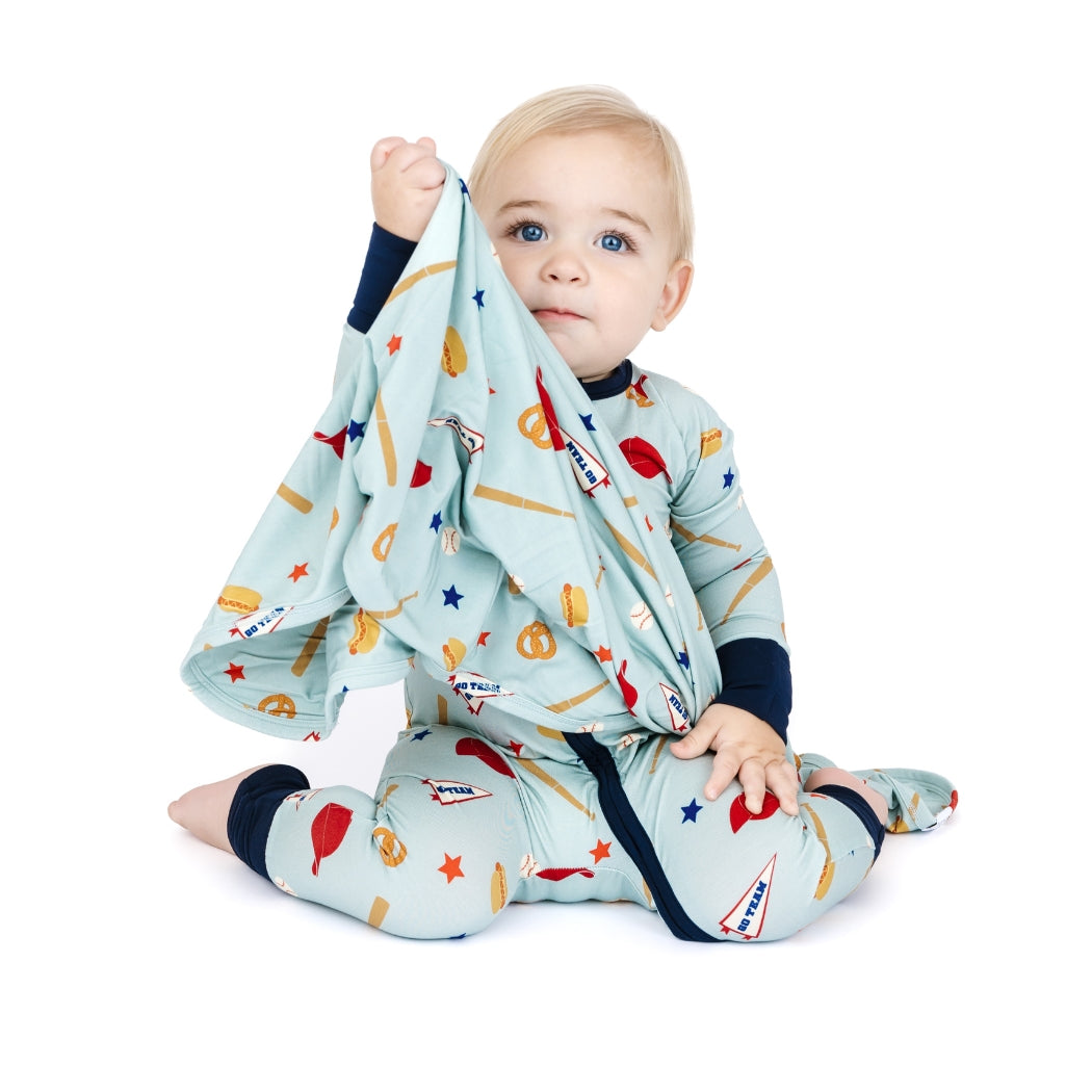Baby in a colorful outfit holding a blanket with various patterns on a white background