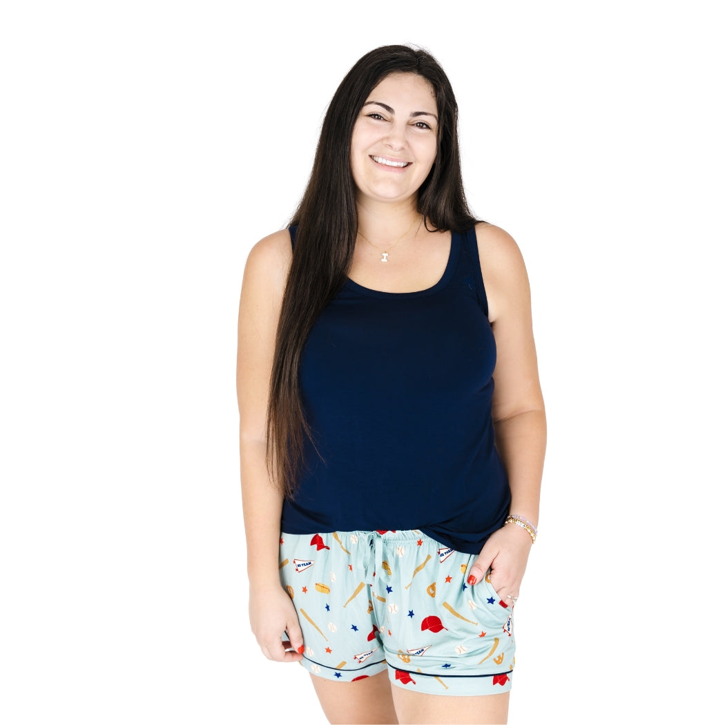 Woman wearing a navy tank top and patterned shorts on a white background