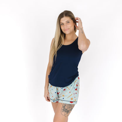 Woman wearing a navy tank top and patterned shorts on a white background