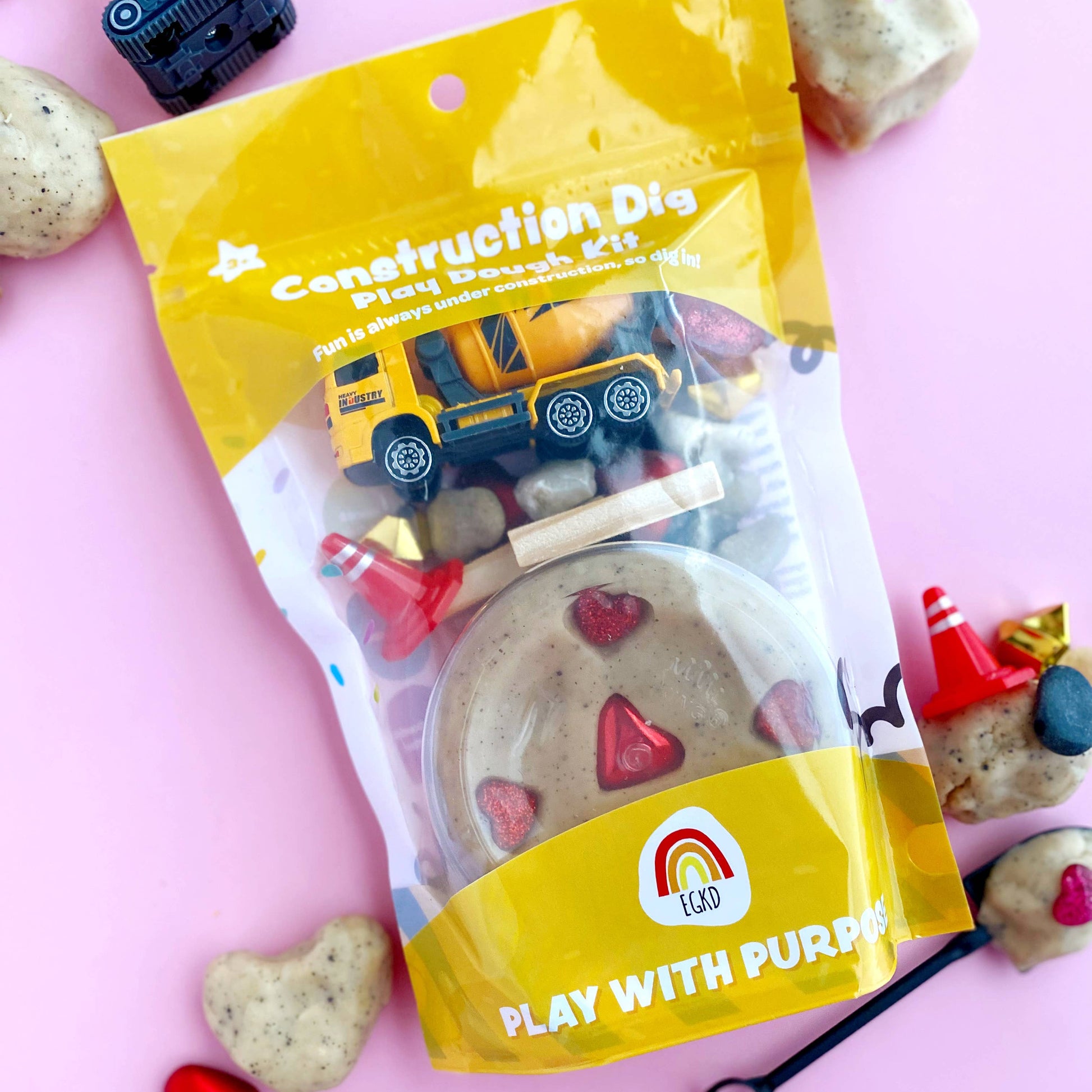 Construction-themed play dough kit packaging with toys on a pink background