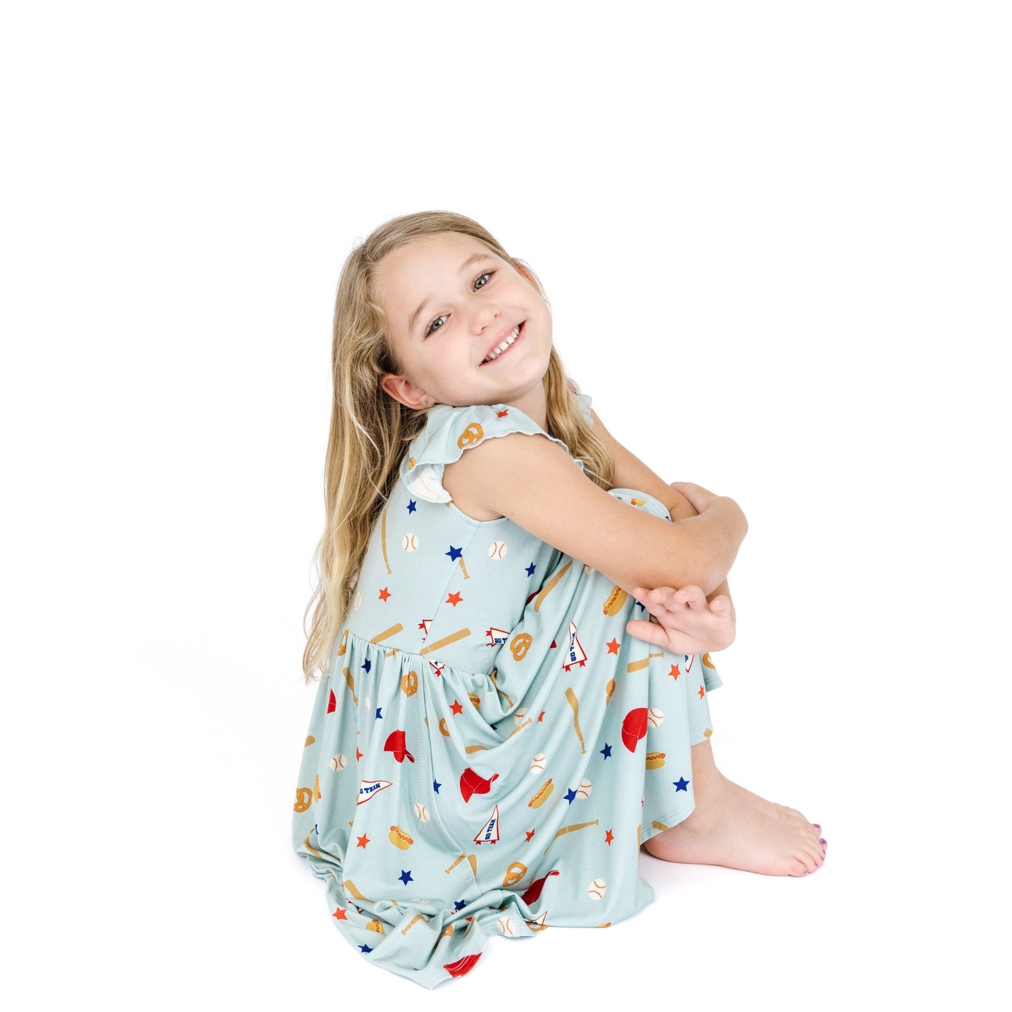 Young girl wearing a light blue dress with sports-themed print on a white background