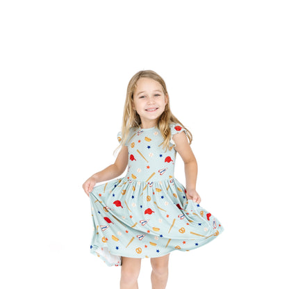 Young girl wearing a light blue dress with sports-themed pattern on a white background