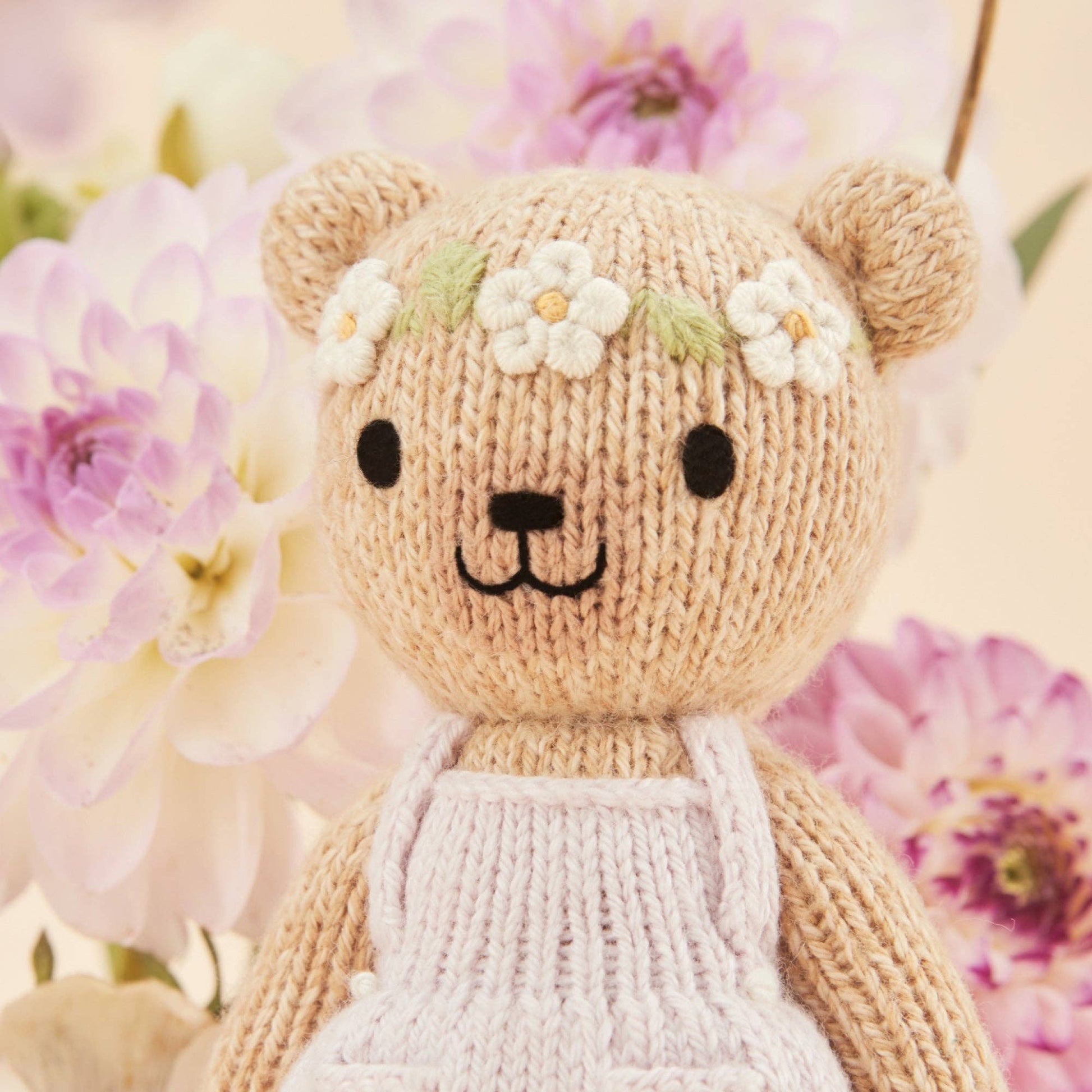 Knitted teddy bear with flower headband in front of flowers