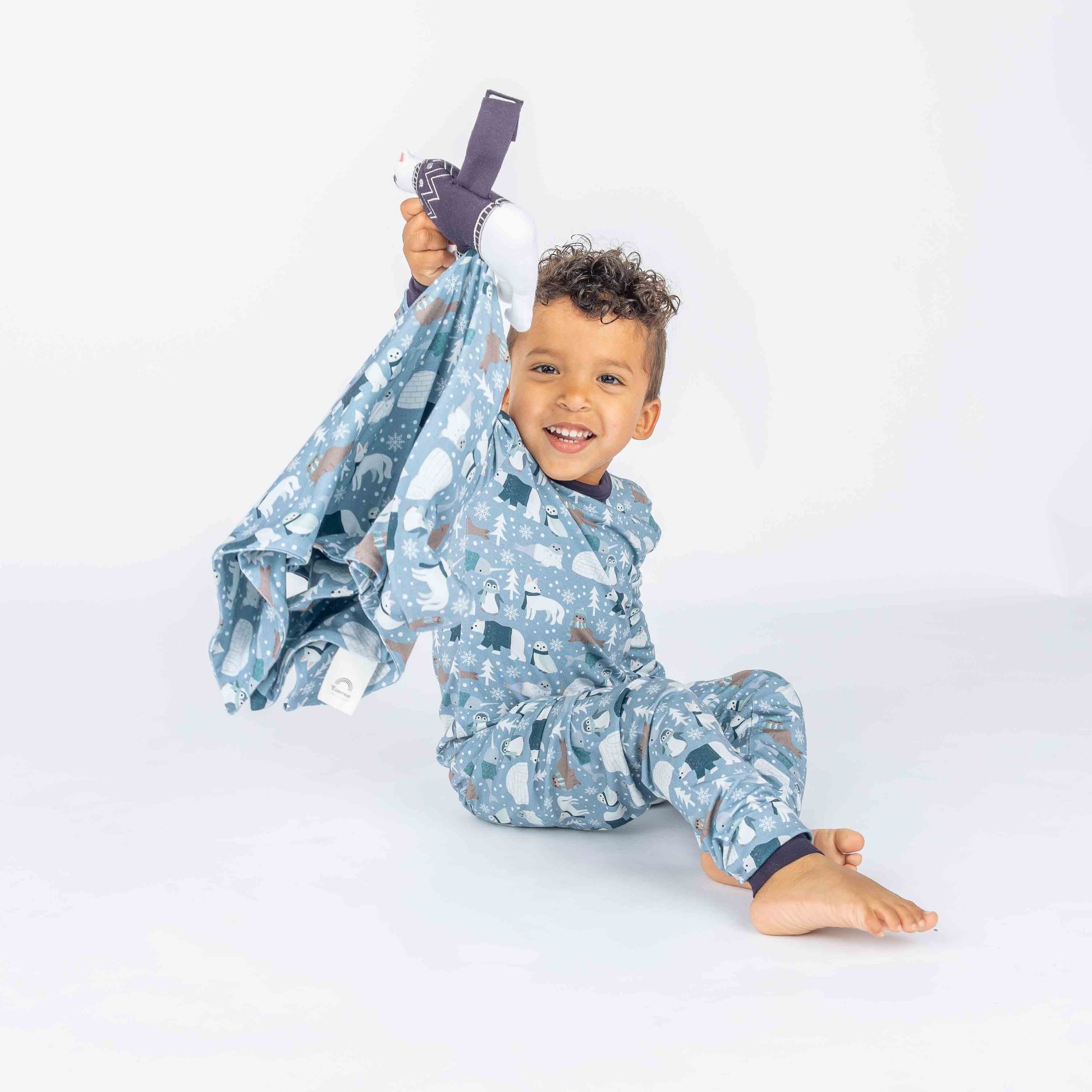 Toddler sitting in white background with polar pals pajamas featuring polar bears holding a Polar bear lovey