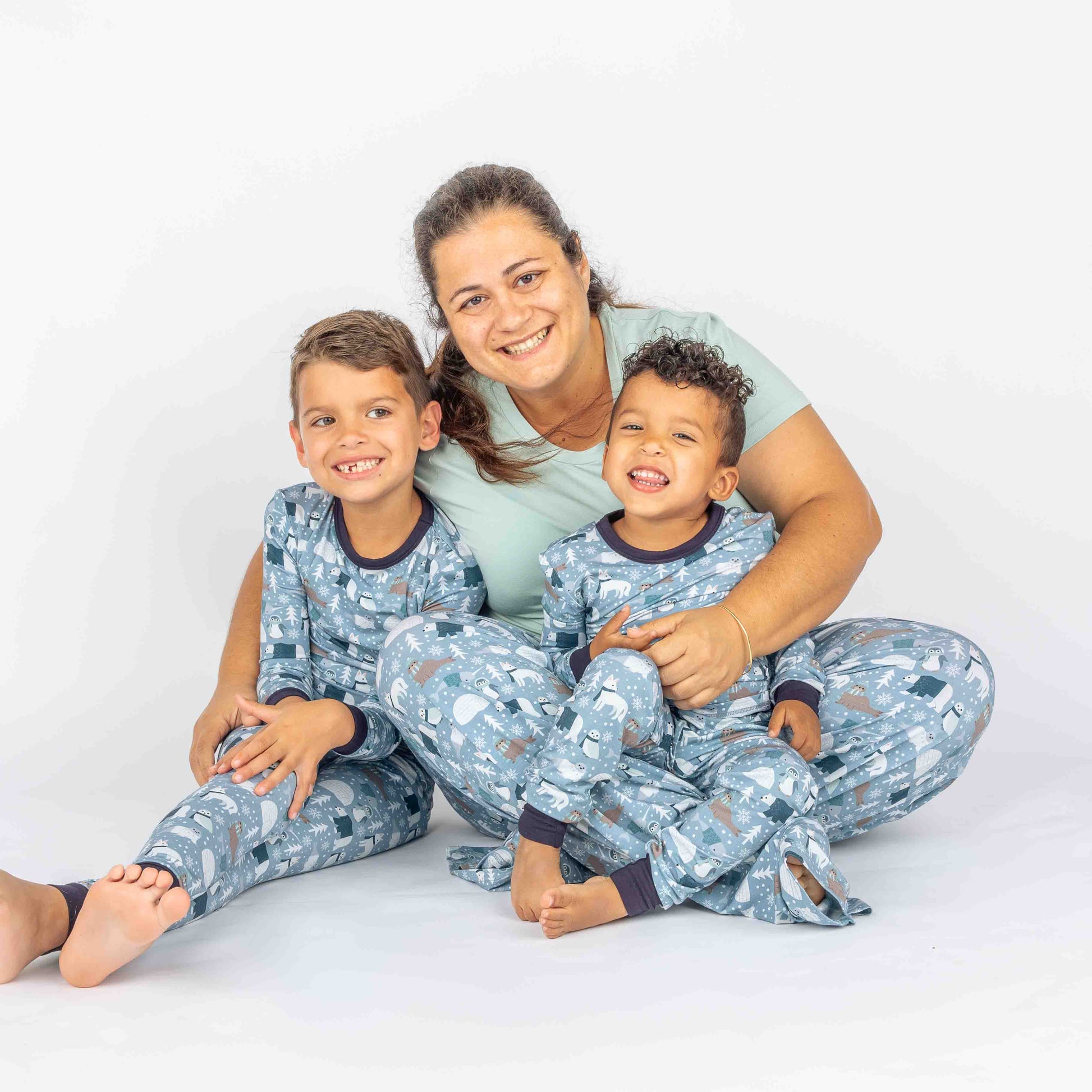 Mother hugging two sons sitting in white background with polar pals pajamas featuring polar bears