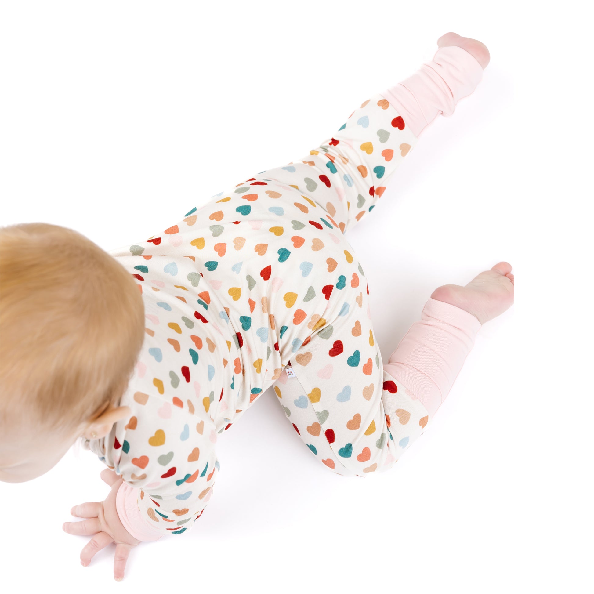 Side view of baby crawling in Rainbow Hearts bamboo footie romper.