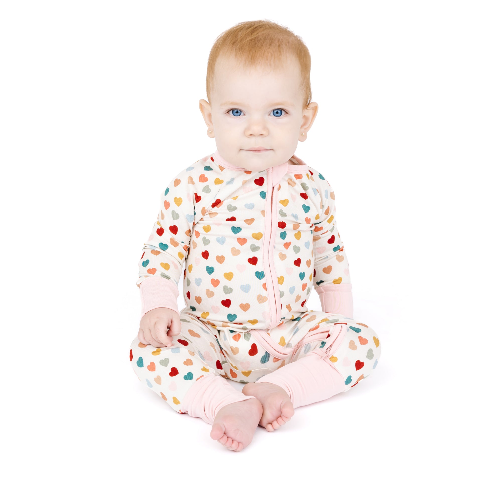 Baby sitting in Rainbow Hearts bamboo convertible footie romper.