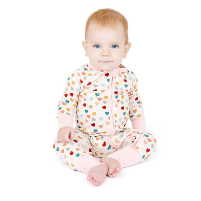 Baby sitting in Rainbow Hearts bamboo convertible footie romper.