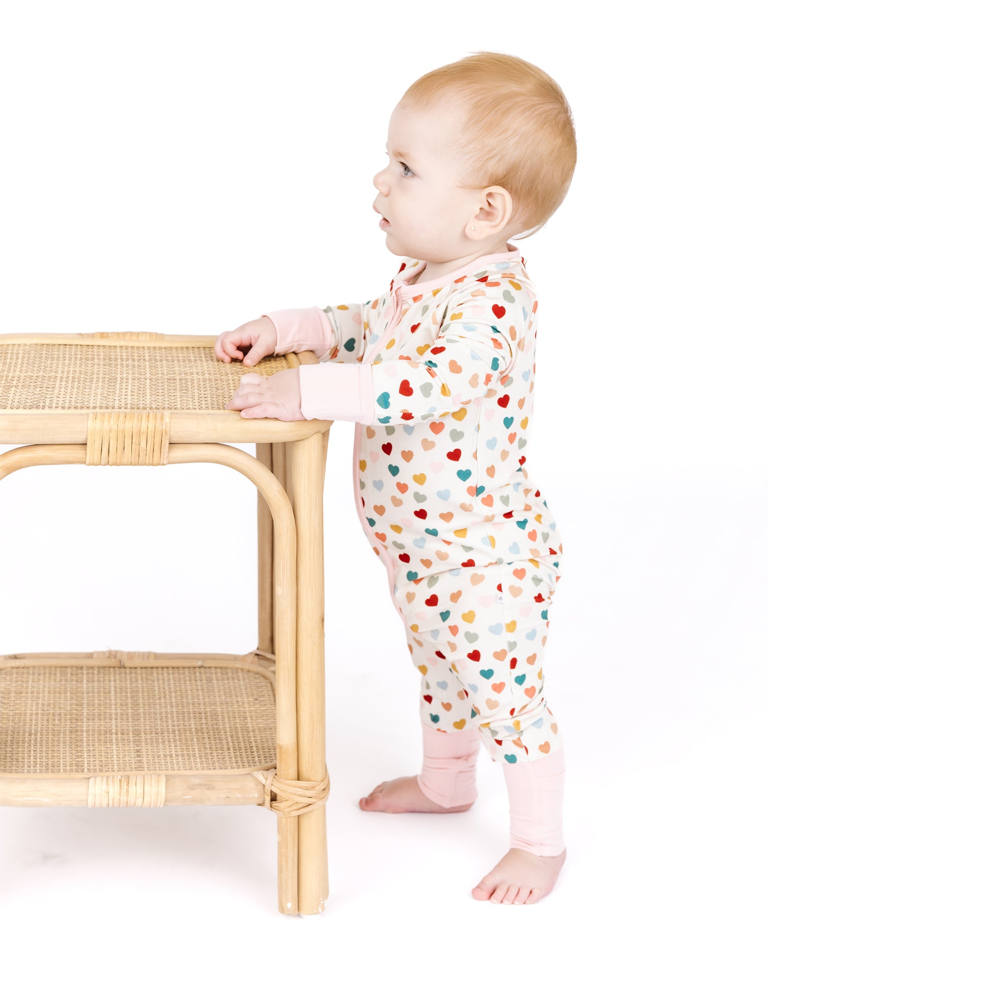 Baby standing in Rainbow Hearts bamboo convertible footie romper.