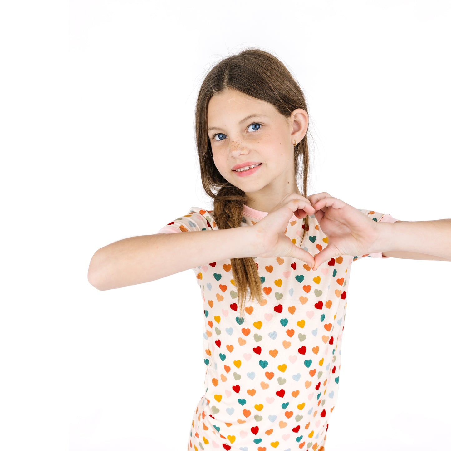 Child wearing Rainbow Hearts bamboo short sleeve pajama set making heart hands.
