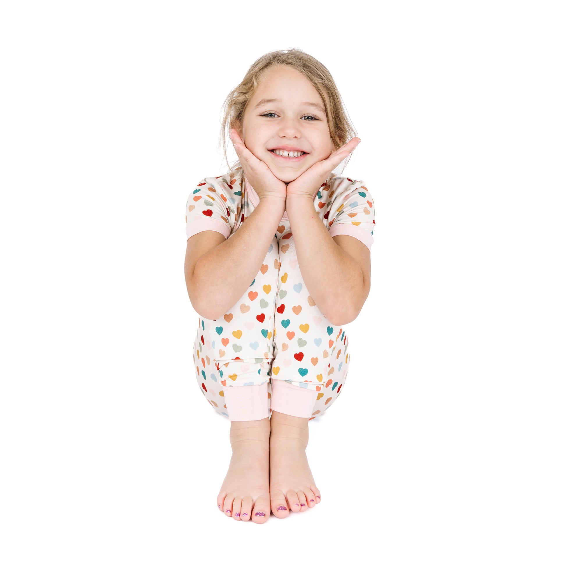 Child sitting in Rainbow Hearts bamboo two-piece pajama set.