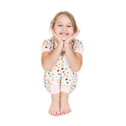 Child sitting in Rainbow Hearts bamboo two-piece pajama set.