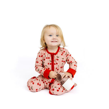 Child wearing a pink onesie with red accents and cherry pattern on a white background