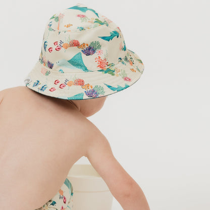 Baby boy wearing and showcasing the back of our Emerson and Friends Coral Reef Reversible Bucket Hat, featuring a vibrant underwater-inspired design with sharks, sea turtles, and coral, offering sun protection and a stylish, adjustable fit for kids and toddlers.