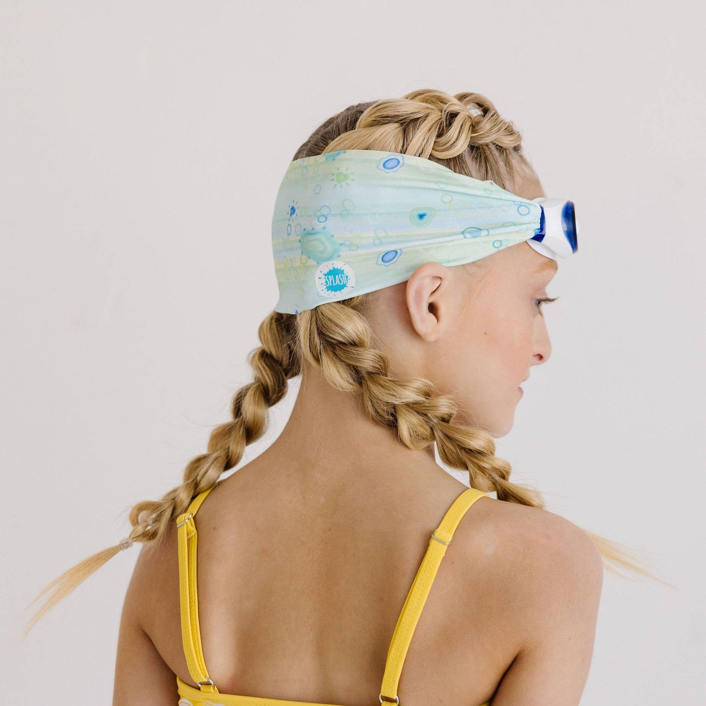 Young girl with braided hair wearing a colorful headband and swimsuit on a plain background