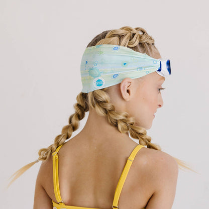 Young girl with braided hair wearing a colorful headband and swimsuit on a plain background