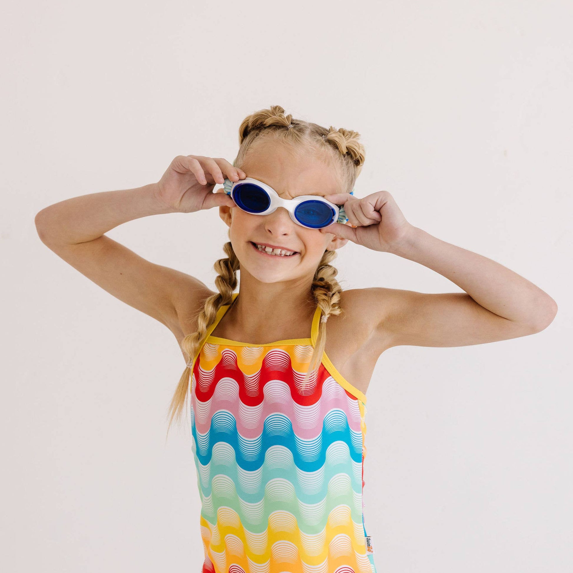Young girl wearing a colorful swimsuit and swim goggles on a plain background