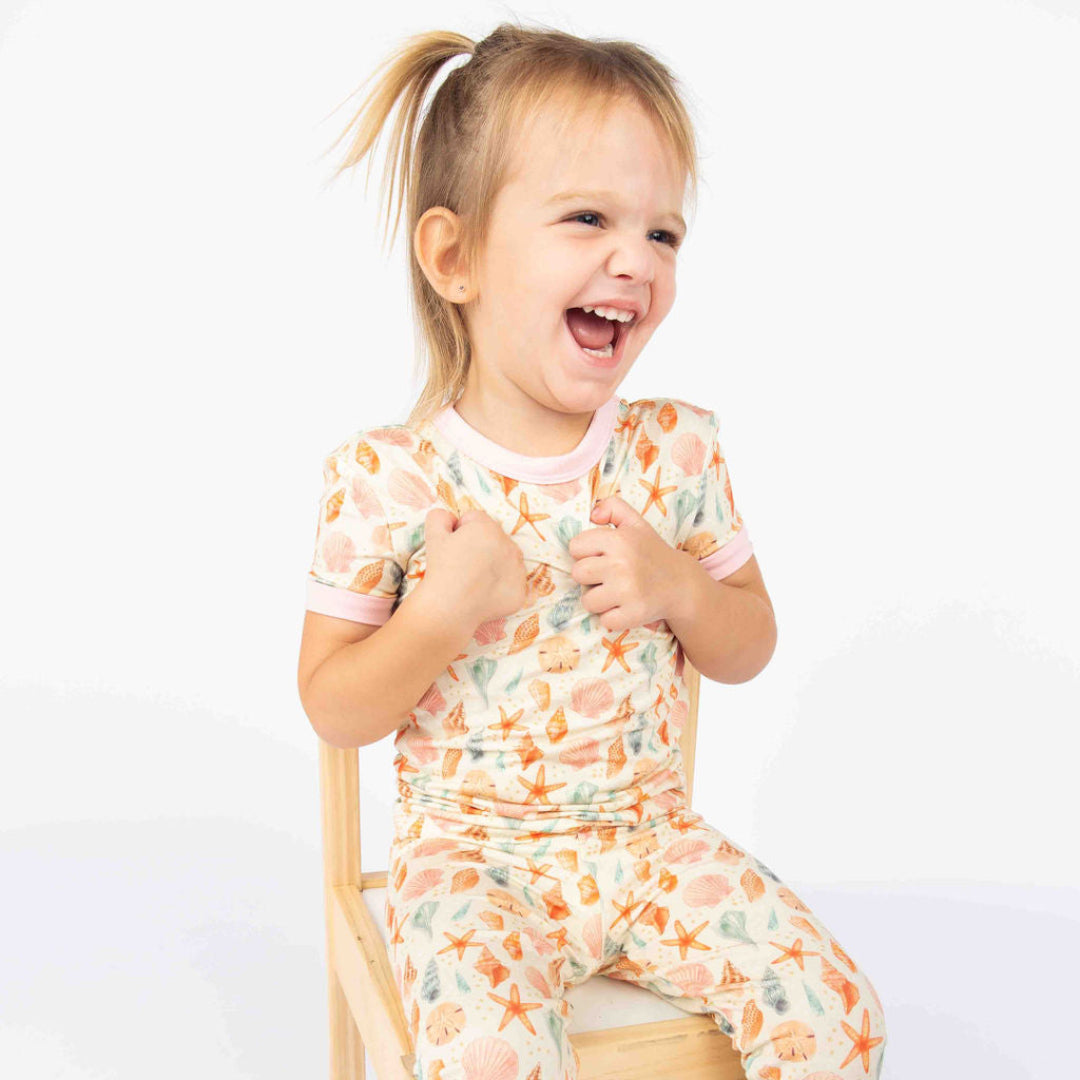 Girl smiling and sitting down in a wood chair with our 2 piece bamboo pajama from our Sandy Shell collection. 