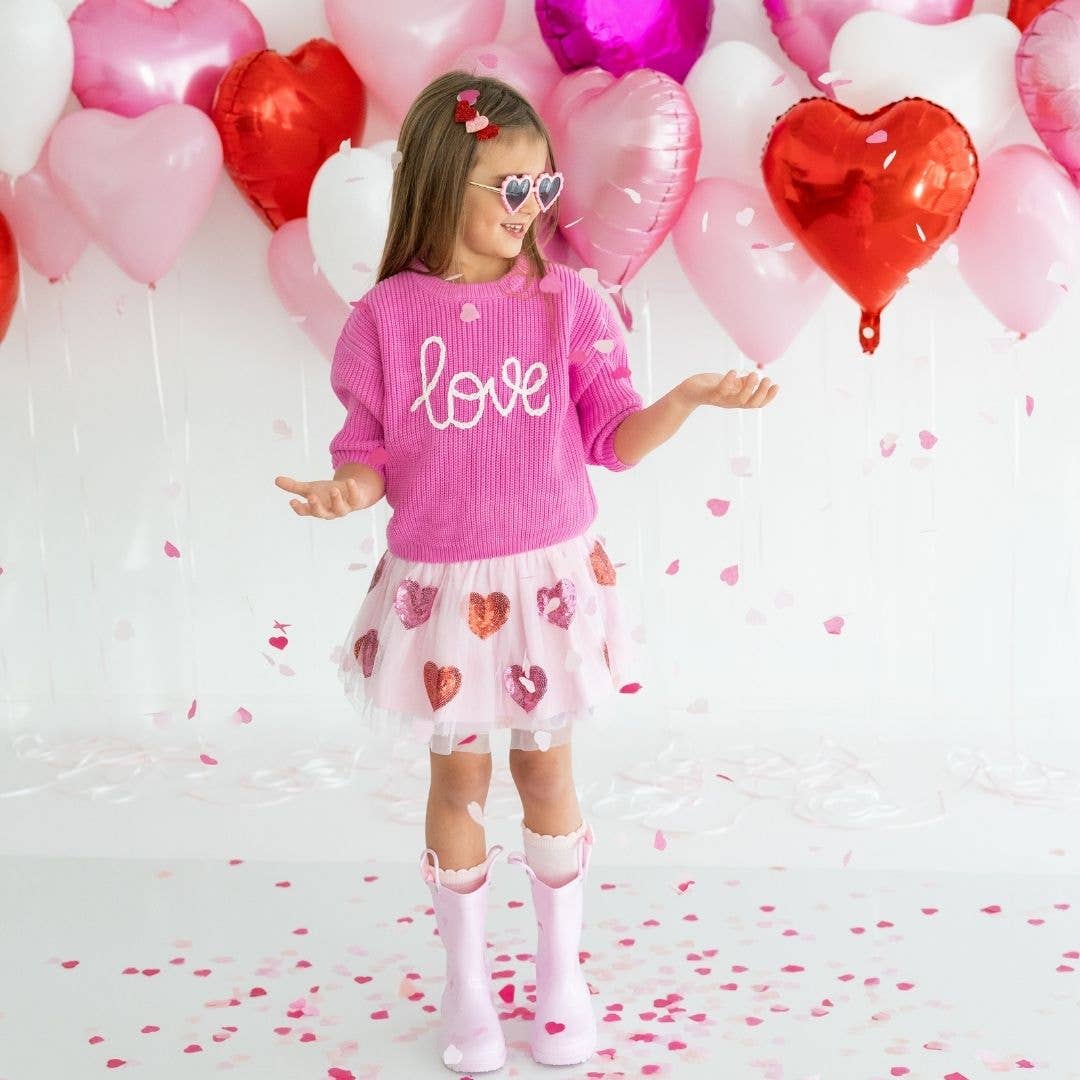 little girl wearing a light pink tutu with dark pink and red sequin hearts on it