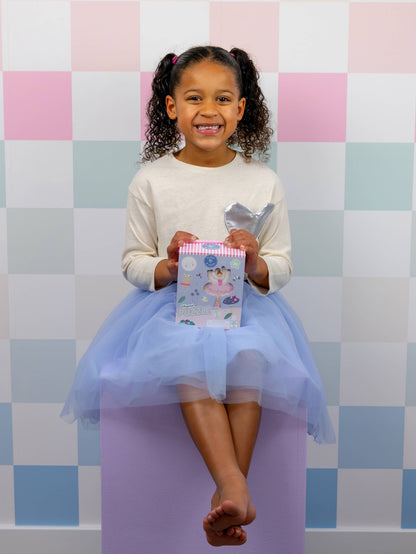 Young girl in a tutu sitting on a purple stool holding a gift box against a checkered background