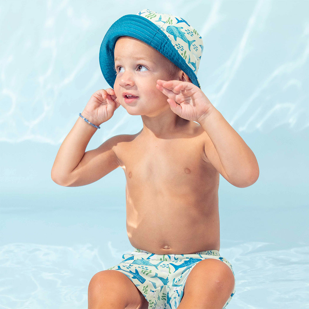 Little boy wearing the Shark Friends Boys Swim Trunks and matching reversible Bucket Hat.