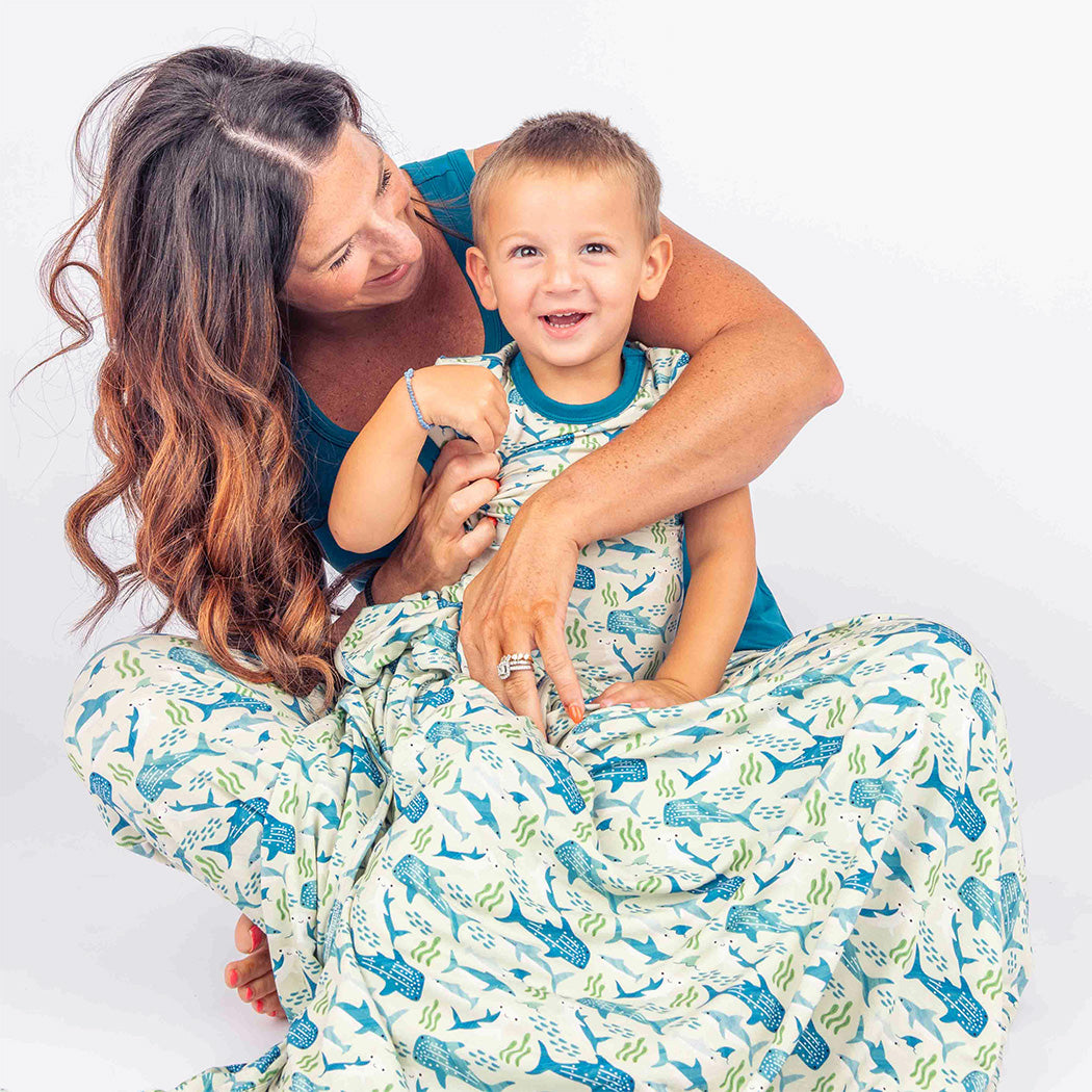 Mom and son wearing our Shark Friends matching Bamboo Pajamas while sitting on the ground wrapped up in our Shark Friends Bamboo Blanket.