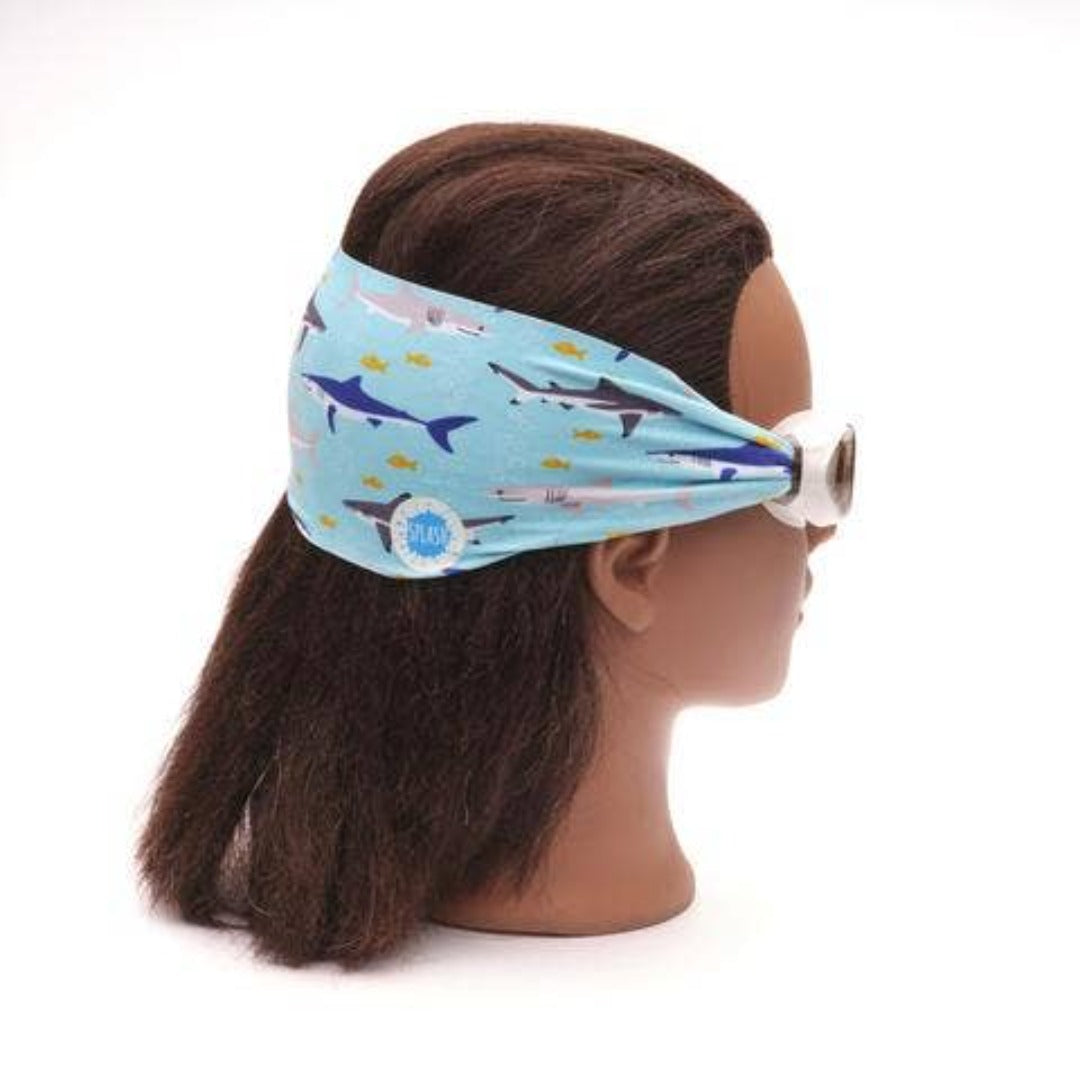 White swim goggles with a blue shark scene strap on a female mannequin head
