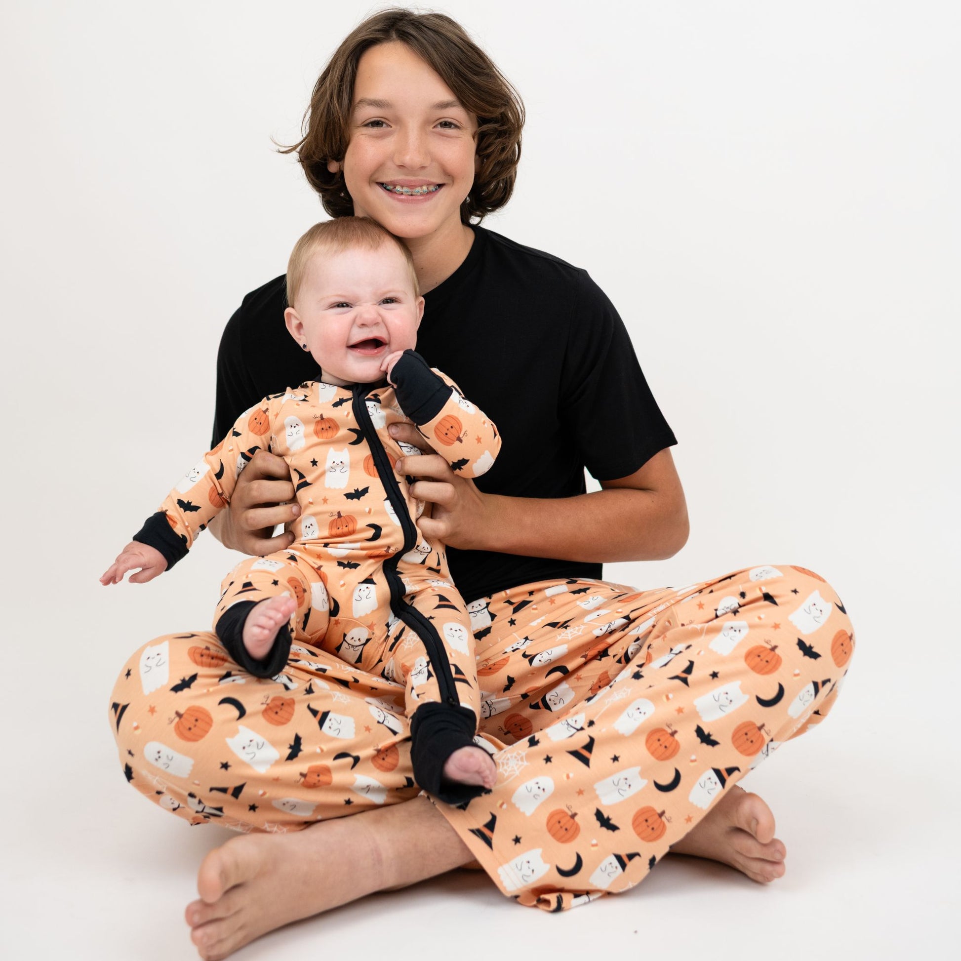 Two children wearing matching Halloween-themed pajamas on a white background , featuring hypoallergenic breathable fabric with ghost and pumpkin print.