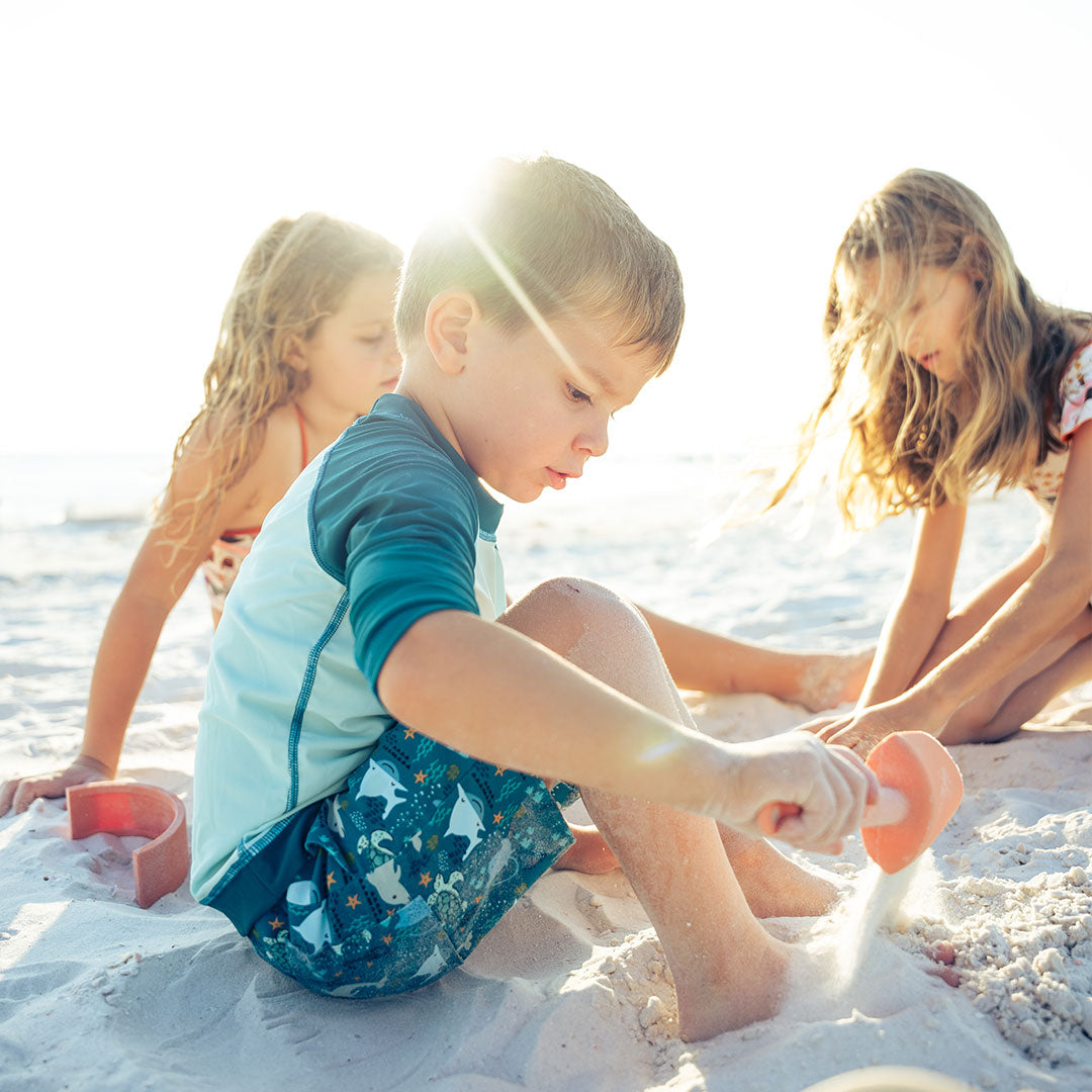 3 children sit and play with the silicone beach bucket toy play set. 