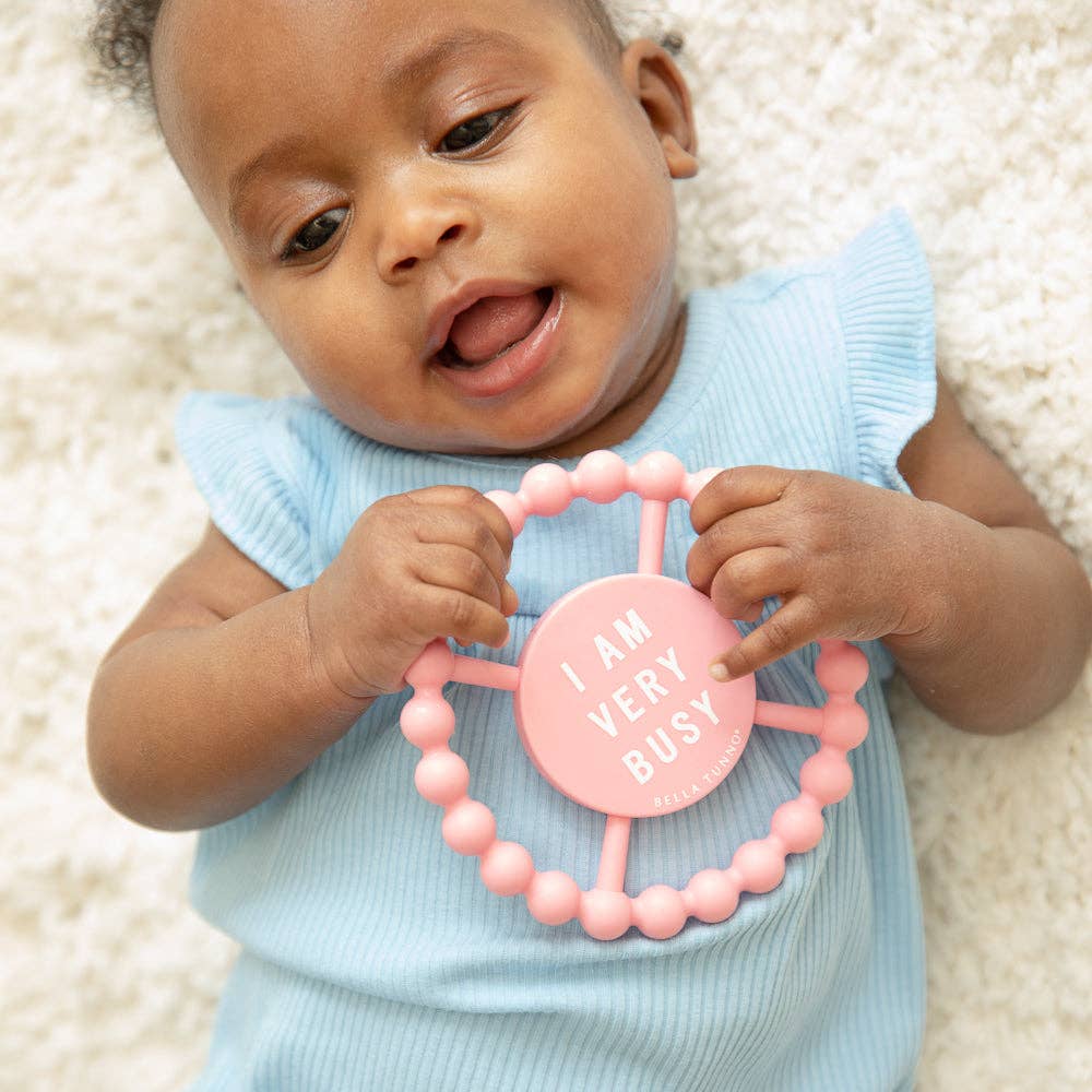 Baby holding a pink teething ring with text on a white background