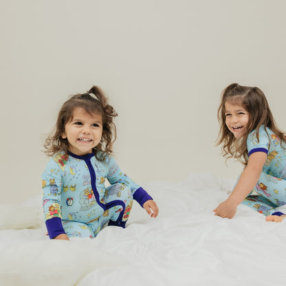 Adorable moment with sisters smiling. She is wearing our collaboration with PBS Good Night Arthur™ pattern. The pajama features Arthur and friends in a cozy bedtime scene with storybooks, toothbrushes, bunny slippers, a sleeping puppy, crescent moons wearing sleep caps, twinkling stars, and the words "GOOD NIGHT!" on a soft blue background.