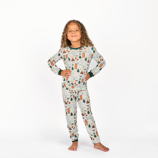 Girl modeling in white background wearing bamboo pajama ski day featuring trees, cabins, and other ski activities.