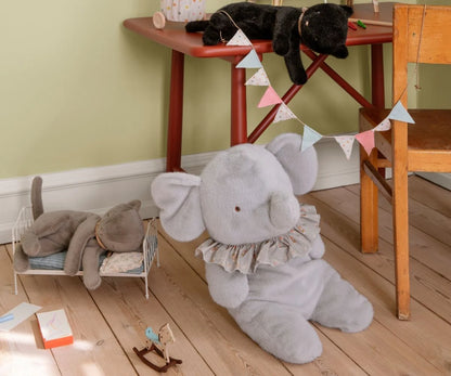Gray elephant plush toy on a wooden floor with a child's play area in the background.