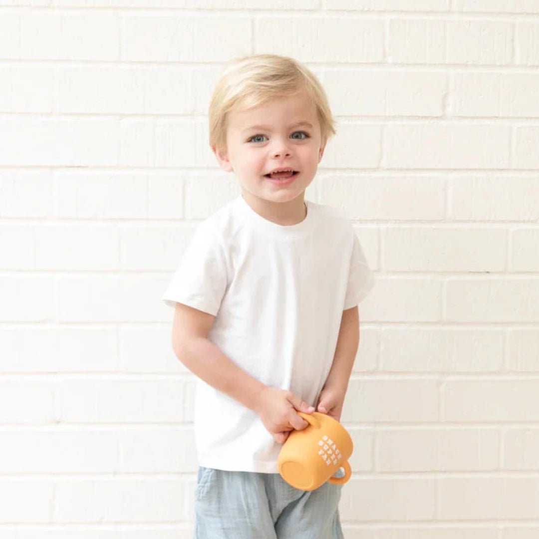 little boy standing holding an orange snack cup that reads snack super fan