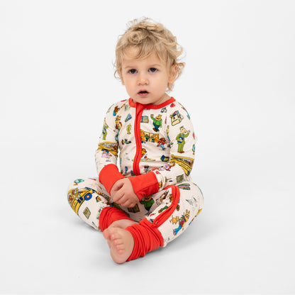 Baby boy wearing our buttery-soft  bamboo convertible pajama featuring red trims and playful illustrations of Arthur™ PBS Character, books, and school bus, a beige background.