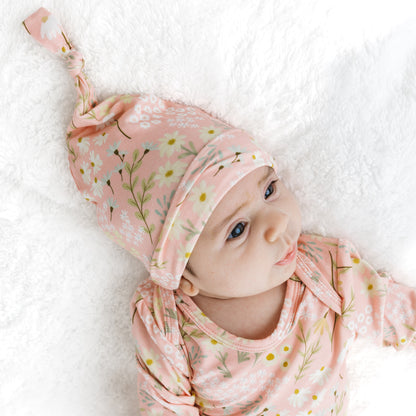 Baby wearing a pink floral hat and matching outfit on a white blanket