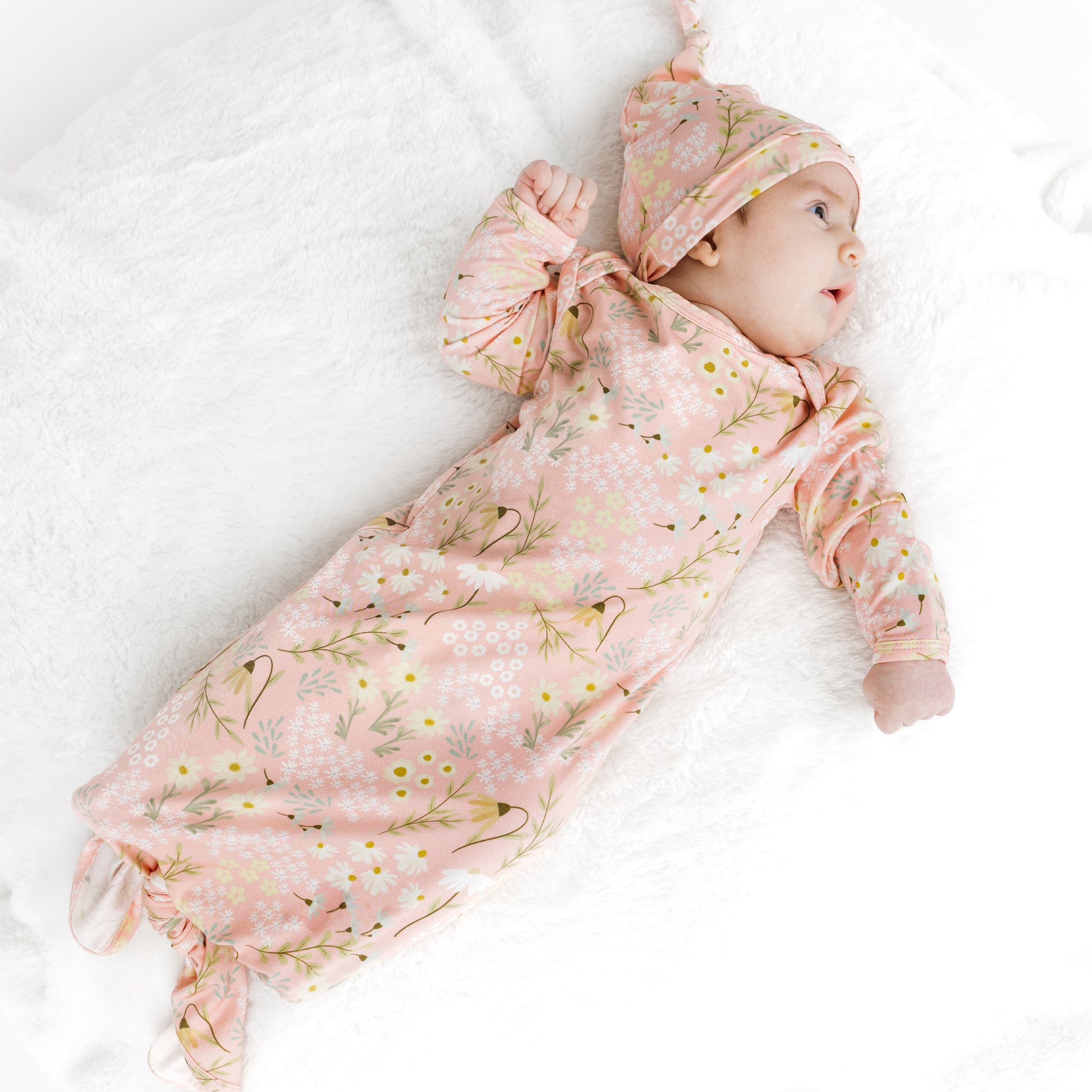 Baby in a pink floral outfit and hat lying on a white blanket