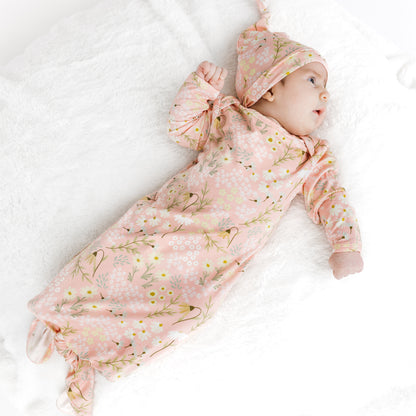 Baby in a pink floral outfit and hat lying on a white blanket