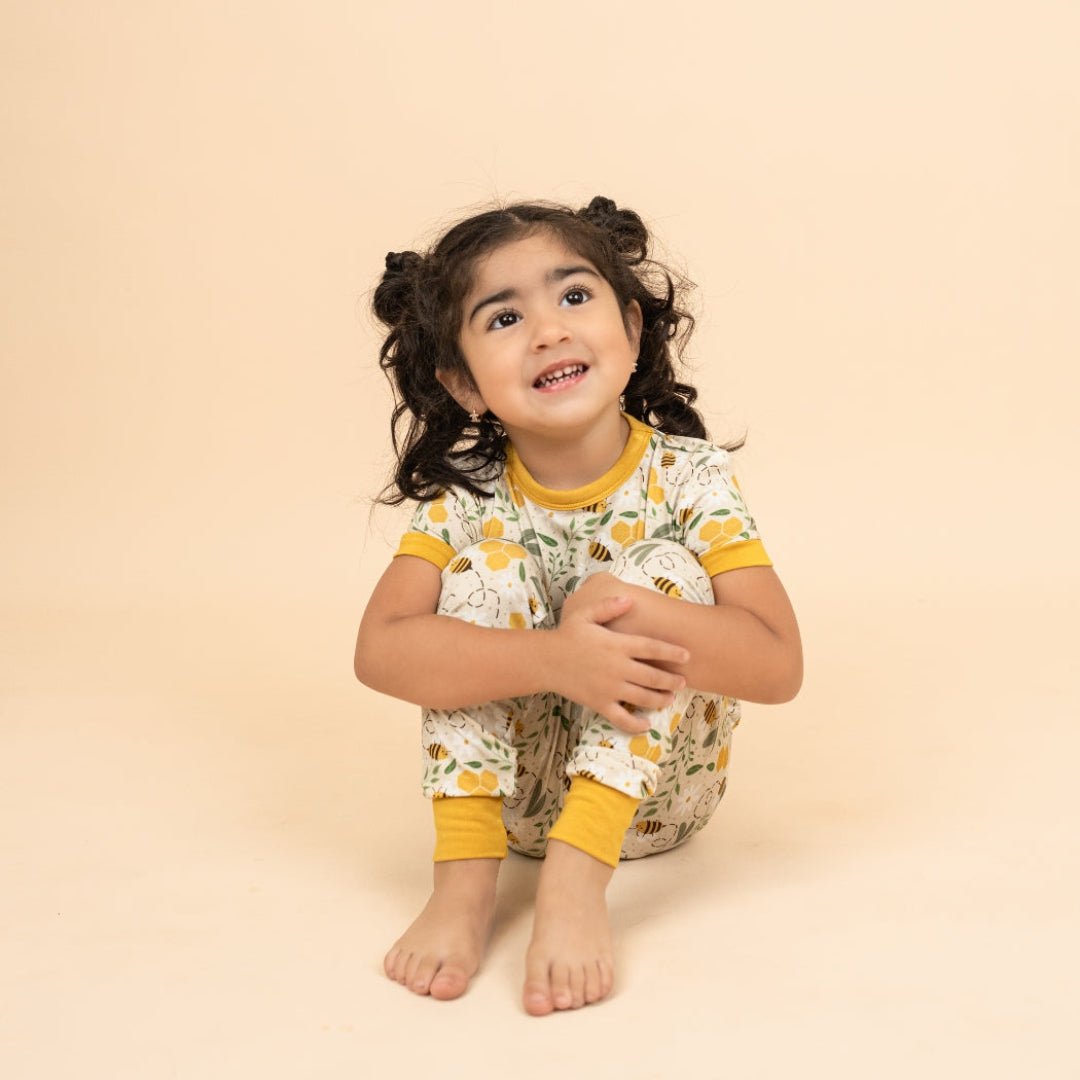 A happy young girl sitting on the floor in lightweight, breathable bamboo pajamas with a spring honey bee and flower print.