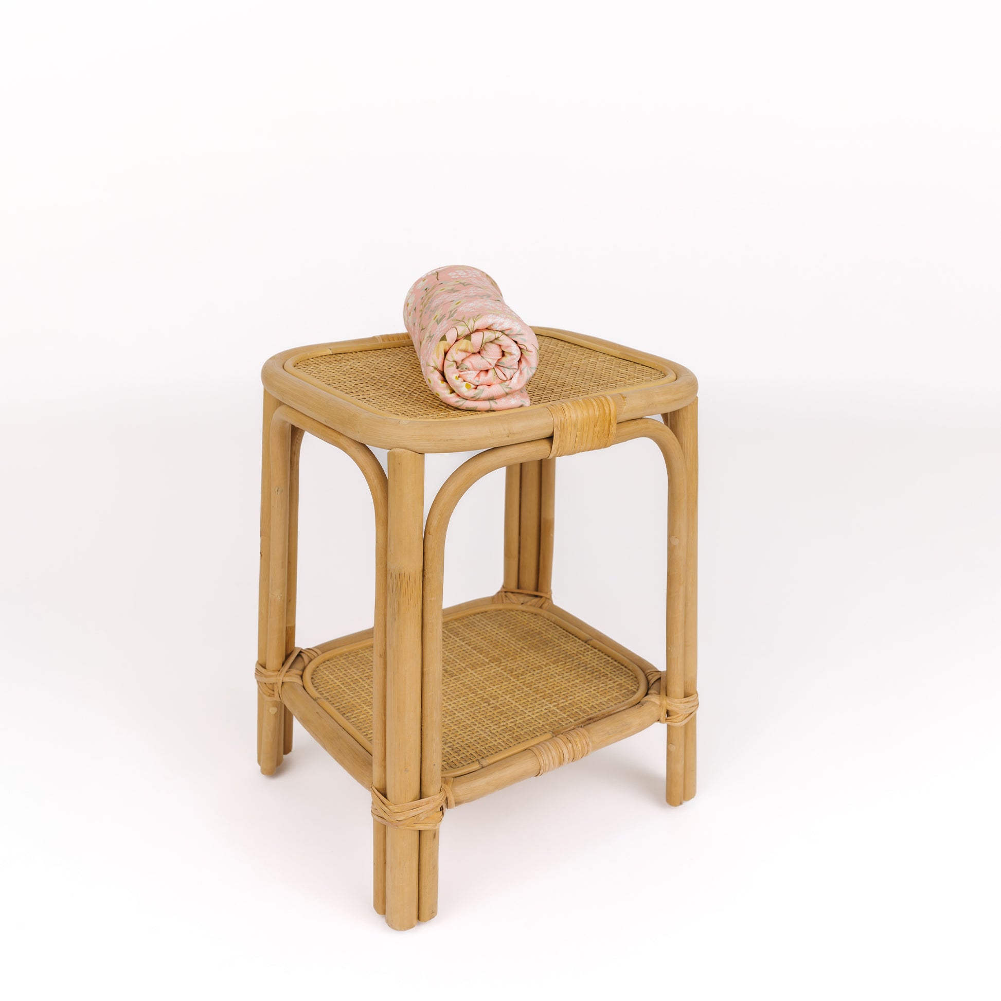 Wicker side table with a rolled-up towel on a white background