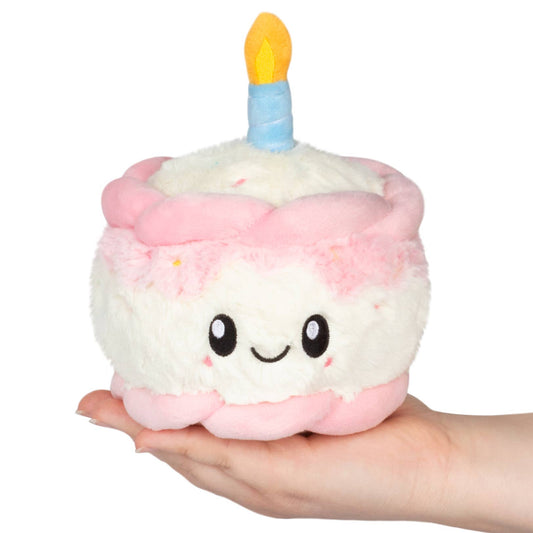 Plush toy shaped like a birthday cake with a candle held in a hand on a white background