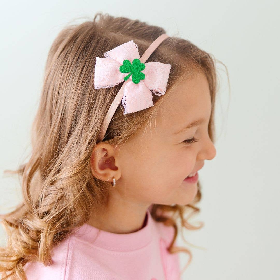 Young girl wearing a pink headband with a shamrock bow on a light background