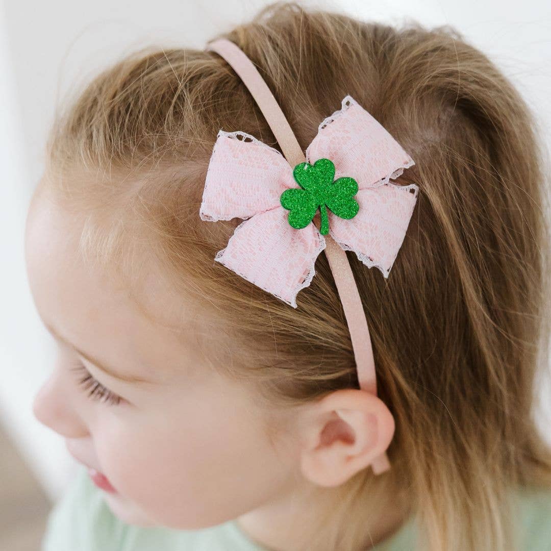 Child wearing a pink bow with a green four-leaf clover on a white background