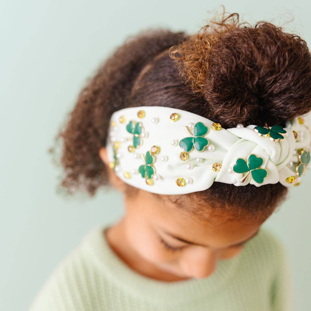 Child wearing a decorative headband with shamrocks and pearls on a light green background
