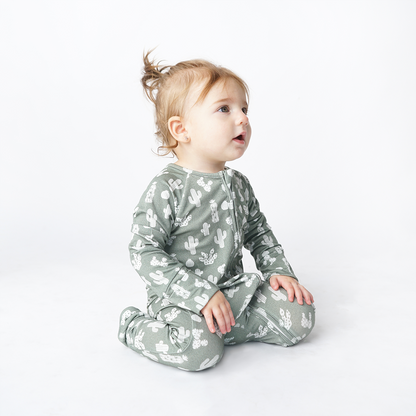 young toddler girl sits on her knees and looks at something behind the camera. she is wearing the "stay sharp" baby convertible. the "stay sharp" print is a variety of different white cacti on a greyish/green background. 