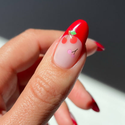 Close-up of a hand with red nail art featuring a cherry design on a blurred background