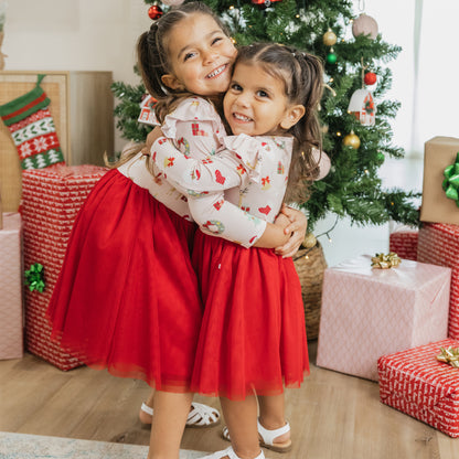 Sisters hugging by the Christmas tree in matching Sugar Plum bamboo tulle dresses, perfect for festive celebrations.
